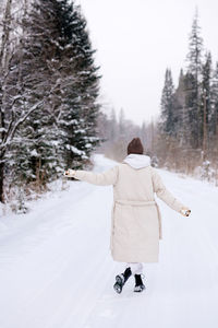 Rear view of woman in warm clothing walking on snow covered landscape. view from behind