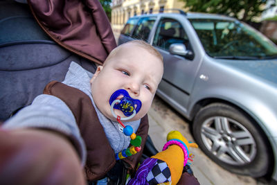 Close-up of baby boy sitting in stroller against car