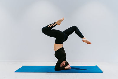 Full length of woman performing headstand against white background