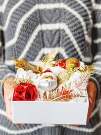 Woman in sweater holds white box with new year decorations. golden decorations for christmas tree.