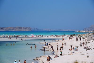 People on beach against clear blue sky