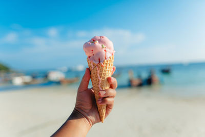 Cropped hand of person holding ice cream cone at beach