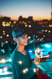 Portrait of smiling man holding camera while standing at night