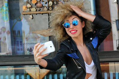 Woman in sunglasses taking selfie through mobile phone outdoors