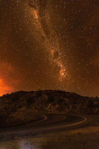 Winding road by hill with stars in sky at night