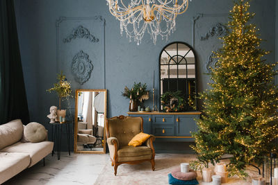 Luxurious living room in blue colors with a christmas tree, an armchair, a sofa and a mirror