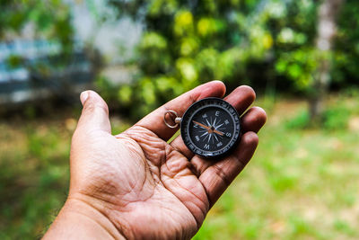 Cropped image of hand holding compass against blurred background