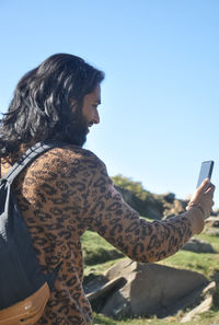 Rear view of a long haired young man taking selfie or having video call with his smartphone 