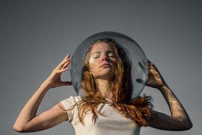 Low angle portrait of young woman wearing glass helmet in head against gray background