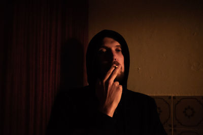 Portrait of man smoking cigarette against wall at home