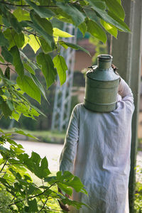 Midsection of man standing by potted plant while carrying a milk container on his back