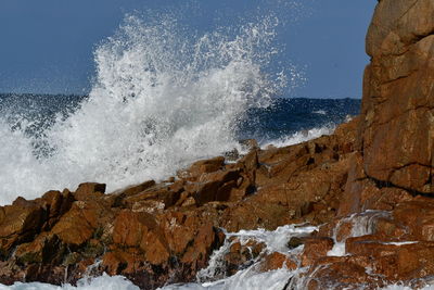 Waves splashing on rocks at shore against sky