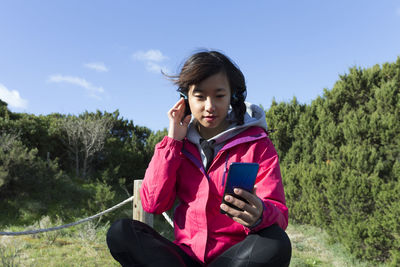 Young chinese woman in the nature using smartphone and listening music