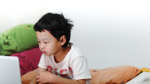 Boy using laptop while sitting on bed at home