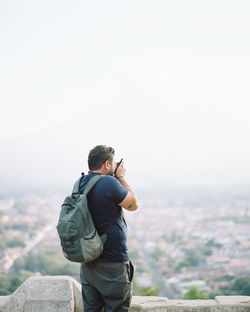 Rear view of man photographing on cityscape against sky