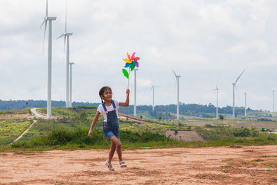 Full length of girl playing with pinwheel toy on land with windmills in background