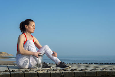 Fit, sporty woman sitting and relaxing after work out beside the sea with a bottle of water.