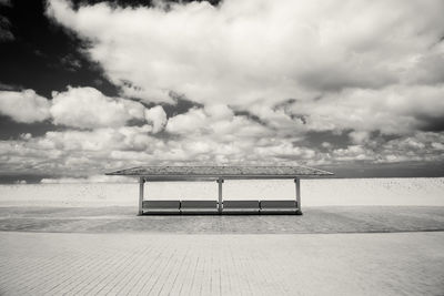 Empty bench by sea against sky