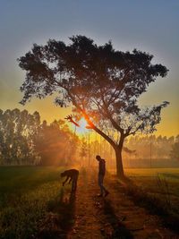 Silhouette people walking on field against sky during sunset