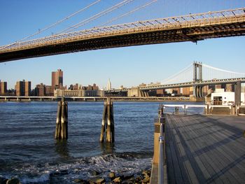 Suspension bridge over river in city against clear sky