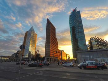 City street by buildings against sky during sunset