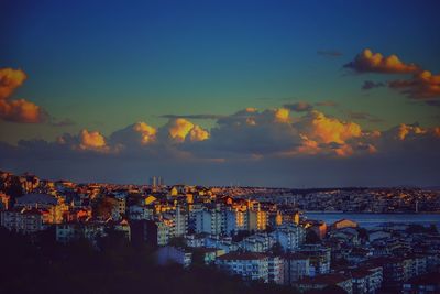 Illuminated cityscape by sea against sky during sunset