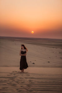 Woman in black dress strolling on sand while spending time in desert in sunrise in doha, qatar