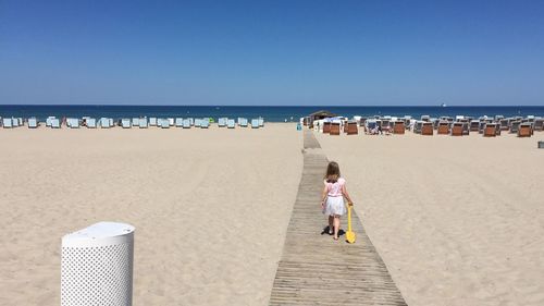 Rear view of girl walking on boardwalk at sandy beach