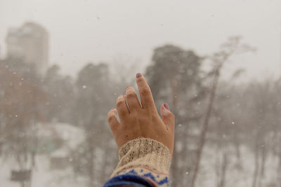 Woman's hand reaches for snowflakes during snowfall with views of nature and houses