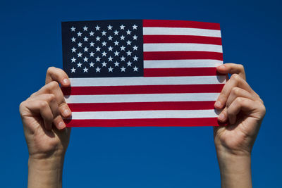 Close-up of hands holding american flag against clear blue sky