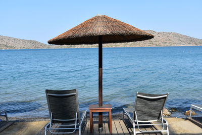 Lounge chairs by sea against clear sky