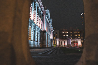 Illuminated road by buildings in city at night