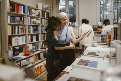 Woman embracing girlfriend buying book from shop