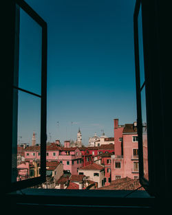 Buildings against clear blue sky seen through glass window