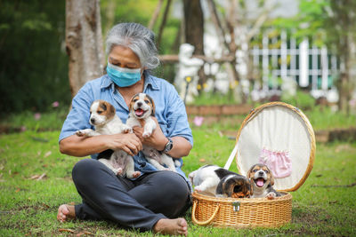 Senior woman wearing mask holding puppies sitting outdoors