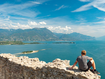 Boy sit alone on rest of manerba castle wall above lago di garda lake. summer holiday and travel