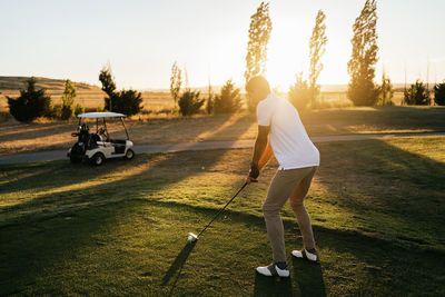 Professional male golf player preparing to hit ball with putter in green field while looking away on summer day