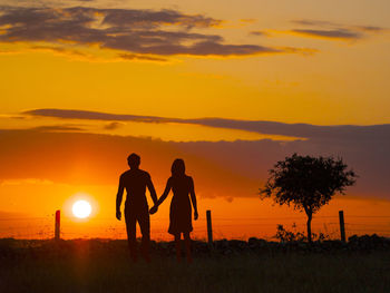 Silhouette couple walking on field against orange sky