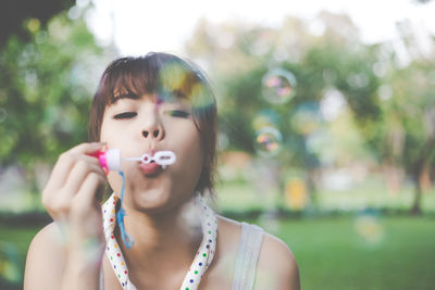 Portrait of young woman blowing bubbles at park