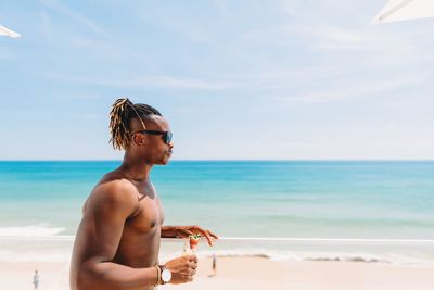 Young man wearing sunglasses at beach against sky