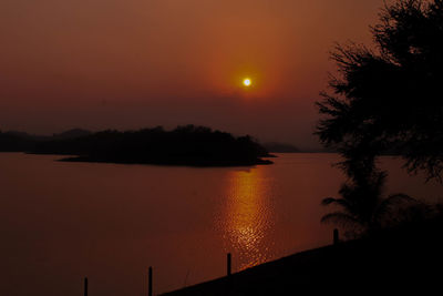 Silhouette trees by lake against sky during sunset