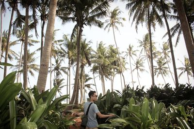 Young man standing against palm trees