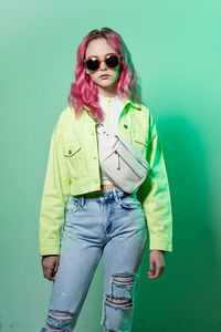 Portrait of young woman wearing sunglasses while standing against blue background