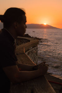 Side view of man looking at sea against sky during sunset