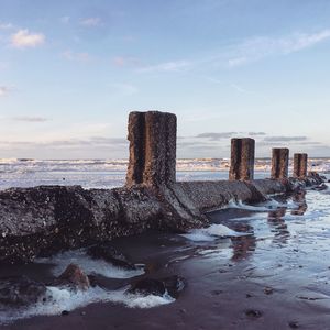 Wooden posts on beach against sky