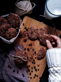 Cropped hand of person holding chocolate chip cookie on cutting board