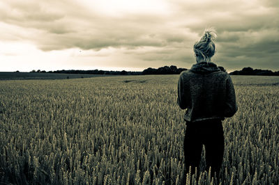Rear view of woman standing amidst crops on field against cloudy sky