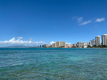 Sea by buildings against blue sky