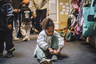 Girl wearing shoe while sitting on carpet at day care center