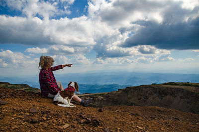 Side view of woman sitting on rock against sky